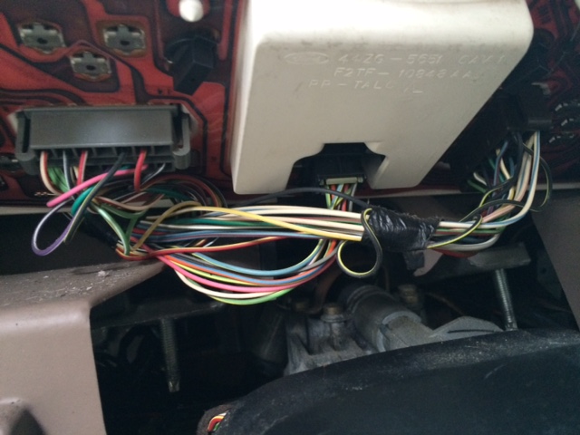 Close-up of a tangled mess of colorful wires connected to a vehicle's dashboard, with some text visible on a white plastic housing