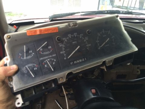 1994 Ford Bronco - Dashboard instrument cluster removed from a vehicle, showing gauges and an orange warning sticker.