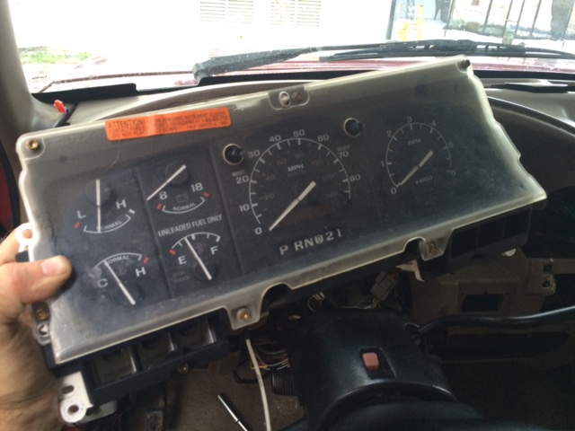 Dashboard instrument cluster with fuel and temperature gauges, speedometer, and tachometer. Orange warning sticker visible