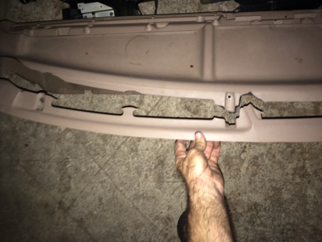 Damaged light brown plastic dashboard trim piece held by a hand.