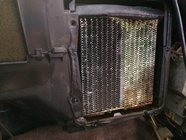 Close-up of a corroded vehicle heater core within its black plastic housing.