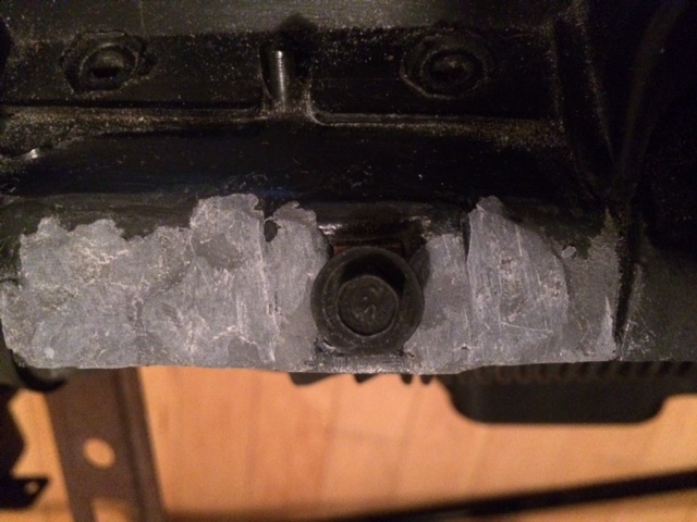 Close-up of a bolt on a black vehicle part with applied grey material.