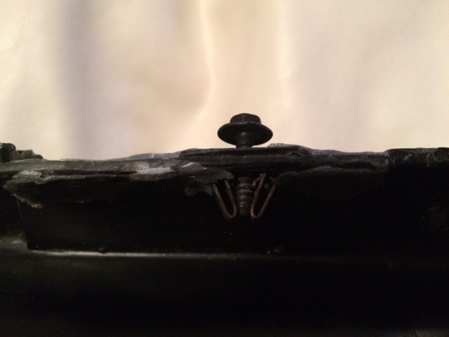Close-up of a screw and metal clips on a black plastic panel.