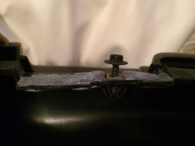 Close-up of a hex bolt and clip on black plastic trim with gray adhesive tape
