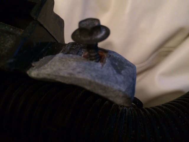 Close-up of a gray metal bracket with a bolt on a black ribbed hose.