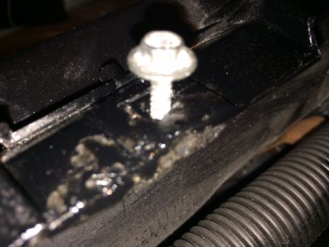 1994 Ford Bronco - A close-up view shows a shiny bolt securing a black plastic component that has a dark, oily residue pooled around it. A ribbed black hose i…