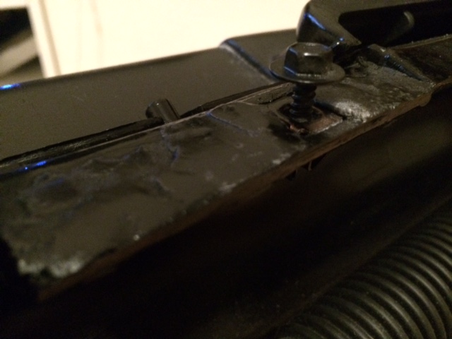 Close-up of a black metal bracket with a hex bolt and washer, showing rust and wear.