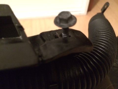 1994 Ford Bronco - A black plastic bracket is secured by a bolt to a ribbed black hose. The bracket has a rectangular cutout and a raised section where the bo…
