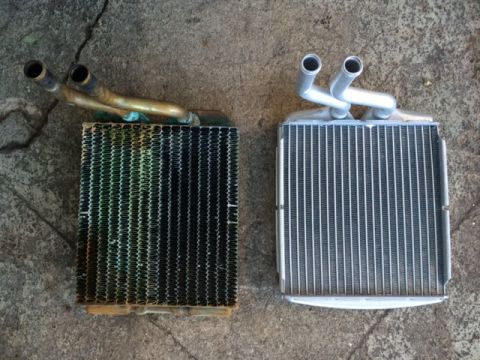 1994 Ford Bronco - Comparison of a used corroded heater core and a clean new aluminum replacement heater core laid on a concrete surface.