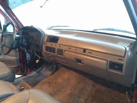 1994 Ford Bronco - The interior of a vehicle is shown, focusing on the dashboard, steering wheel, and driver's side door panel. The dashboard is a neutral bei…