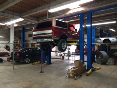 1994 Ford Bronco - A red and tan Ford Bronco is raised on a two-post car lift in a garage. To the right, a silver sports car is also on a lift.