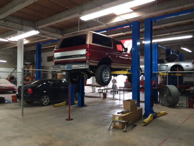 Red and tan Ford Bronco on a car lift in a garage.