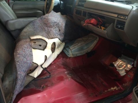 1994 Ford Bronco - The interior of a red Ford Bronco is shown with the passenger side floor exposed, revealing rust and damage. A large piece of the carpet an…