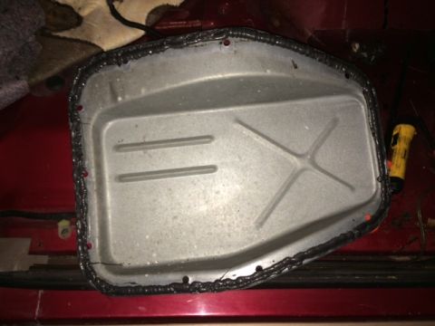 1994 Ford Bronco - A metal oil pan with a black sealant applied around the rim is shown, resting on a red surface. The pan has internal bracing and several bo…
