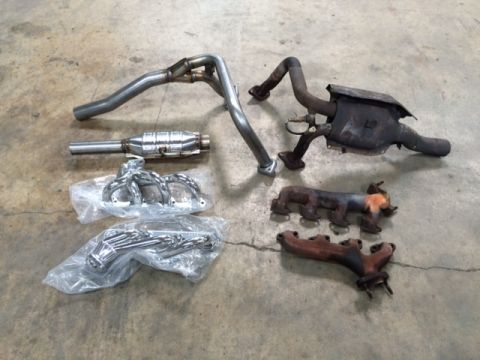 1994 Ford Bronco - Various exhaust system components, including catalytic converters and exhaust manifolds, are laid out on a concrete floor.