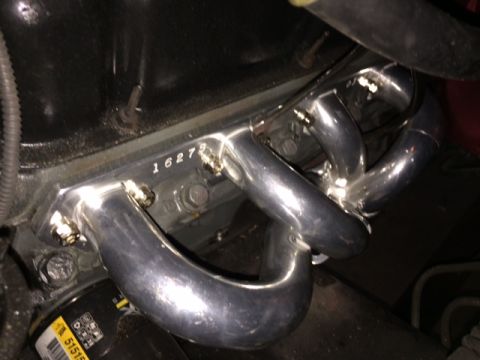 1994 Ford Bronco - A close-up view of a shiny chrome exhaust manifold bolted to a dark engine block. The manifold has four distinct pipes that merge together.