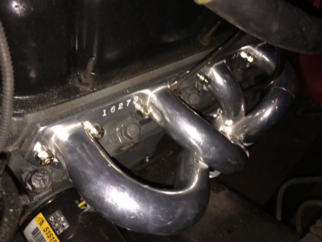 Shiny chrome exhaust manifold bolted to a dark engine block.