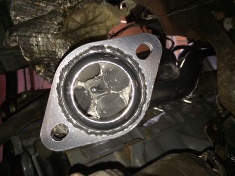 1994 Ford Bronco - A close-up view of a chrome exhaust manifold flange with gasket material visible. The flange is attached to a vehicle's engine block, with…
