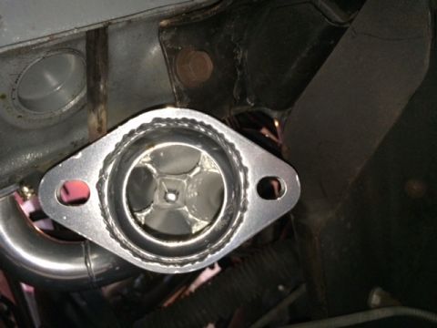 1994 Ford Bronco - A close-up view of a custom exhaust manifold flange with a metallic finish, attached to a vehicle's engine block. The flange has a unique i…