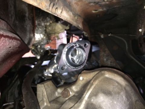 1994 Ford Bronco - A close-up view of a shiny metal exhaust manifold flange with a gasket attached, seen from underneath a vehicle. The flange appears to be p…