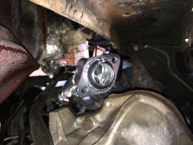Close-up of shiny exhaust manifold flange with gasket, under a vehicle.