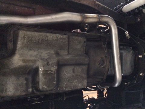 1994 Ford Bronco - The underside of a vehicle shows the transmission pan and exhaust system. A shiny metal exhaust pipe curves around the transmission.