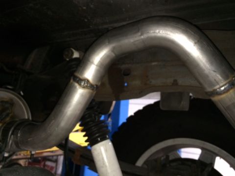 1994 Ford Bronco - A close-up view shows the underside of a vehicle, focusing on a custom exhaust system with visible welds. A portion of a tire and suspensio…