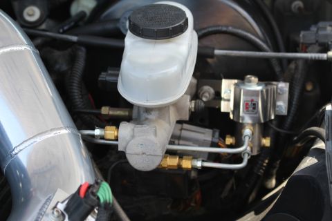 2003 Ford Crown Victoria - Photo of a brake master cylinder with translucent reservoir and metal brake lines in an engine bay.