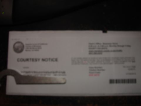 1973 Ford Ranchero - A close-up, blurry shot of a white document labeled "COURTESY NOTICE" is shown. A metal tool, possibly a wrench, is partially visible in th…