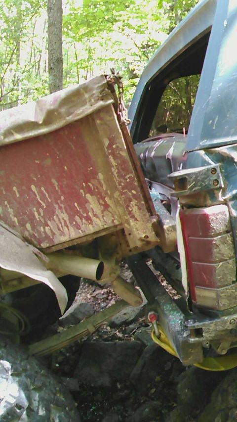 1988 Ford Bronco - A close-up, low-angle view of the rear of a heavily modified, possibly damaged, dark-colored vehicle, featuring a red, mud-splattered dump…