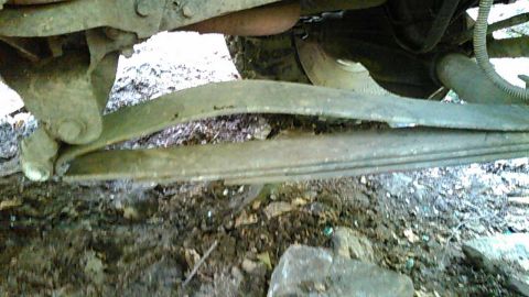 1988 Ford Bronco - The underside of a vehicle shows a damaged leaf spring assembly. The spring appears to be bent and possibly broken.