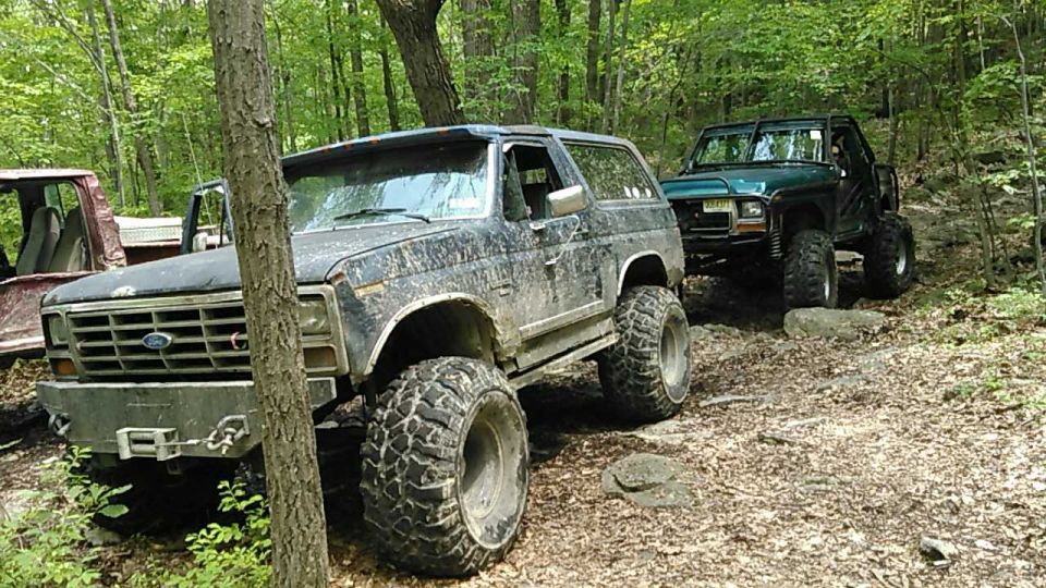 Two modified Ford Broncos on a wooded trail.