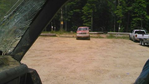 1988 Ford Bronco - A tan Ford pickup truck is parked in a dirt lot facing forward, with a forest in the background. A white pickup truck with a trailer is par…