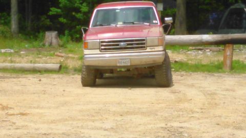 1988 Ford Bronco - Front view of a lifted red Ford Bronco with large tires parked on a dirt surface. The license plate reads "YDZ-6423".