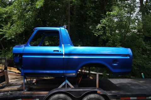 1979 Ford Bronco - The blue painted body of a 1979 Ford Bronco is shown from the side, mounted on a trailer. The vehicle is missing doors, windows, and other…