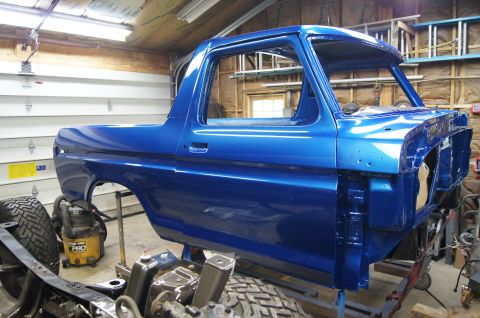 1979 Ford Bronco - A bright blue, partially restored Ford Bronco is shown in a garage setting. The vehicle is on a stand with the front end disassembled, reve…