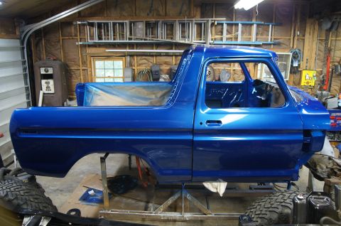 1979 Ford Bronco - A bright blue Ford Bronco body is on a stand in a garage, with the interior and bed visible. The vehicle is undergoing restoration, with to…