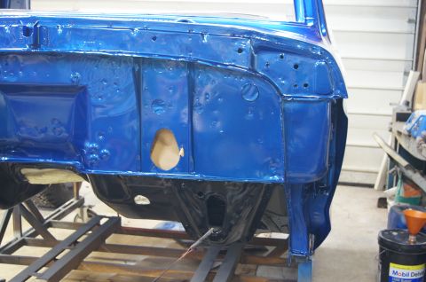 1979 Ford Bronco - The blue painted firewall and inner fender well of a classic vehicle are shown, mounted on a metal stand in a workshop. The area appears to…