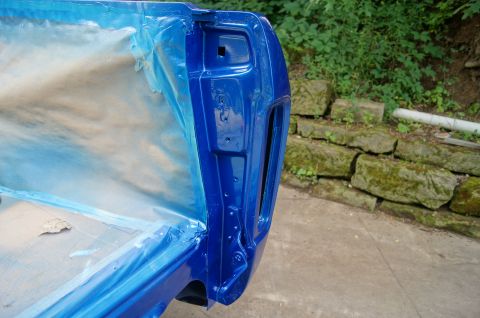 1979 Ford Bronco - The corner of a blue vehicle's body, likely a truck bed or tailgate, is shown with blue masking tape and paper protecting the interior. The…