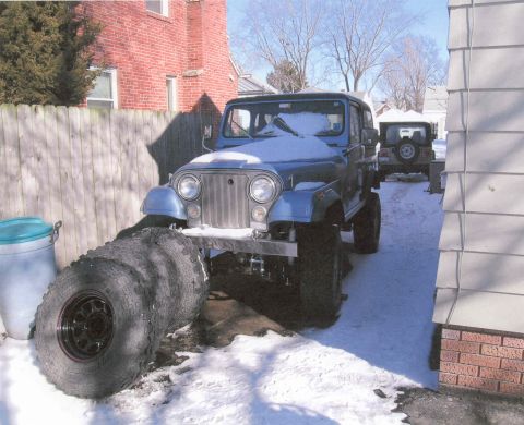 1984 Jeep Wrangler - A blue Jeep CJ is parked in the snow with several tires stacked in front of it.
