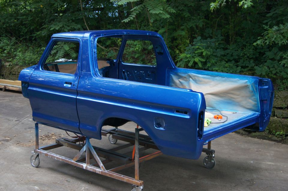 1979 Ford Bronco body, painted blue, on a wheeled stand outdoors.
