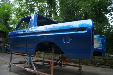 1979 Ford Bronco - A bright blue, classic pickup truck bed and cab are mounted on a metal stand with wheels. The vehicle appears to be undergoing restoration…