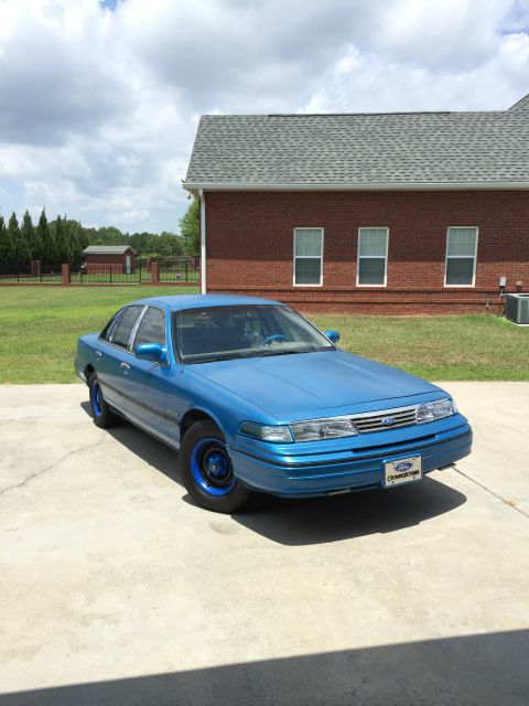 1994 Ford Crown Victoria - This blue 1994 Ford Crown Victoria is parked in a driveway with a brick house in the background.