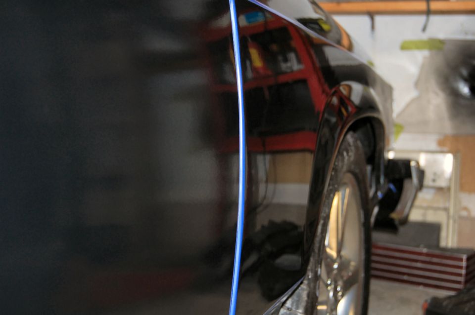 Side view of a black car's rear fender and door with blue pinstripe.
