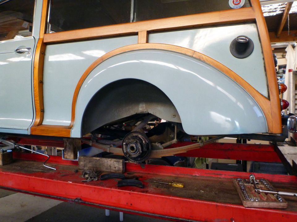 Rear wheel well of a classic light blue station wagon with wood trim on a red lift.