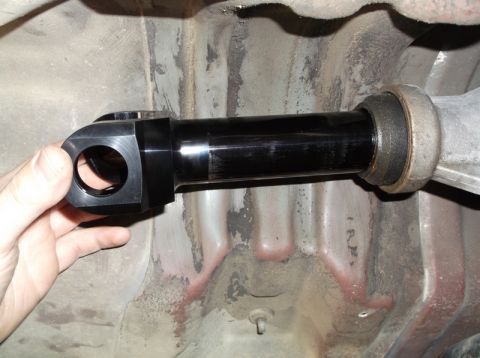 1999 Mercury Grand Marquis - A close-up view of a black, aftermarket driveshaft component being held by a hand under the chassis of a vehicle. The part connects to a si…