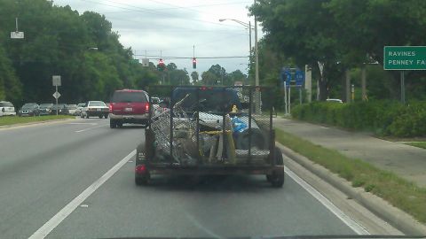 1994 Ford Bronco - A red Ford Bronco is seen from the rear, driving on a road behind a trailer loaded with various items. The trailer is attached to a blue pi…