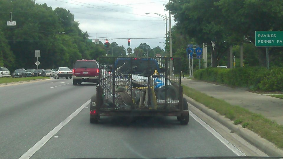 Red Ford Bronco driving on a road behind a loaded trailer.