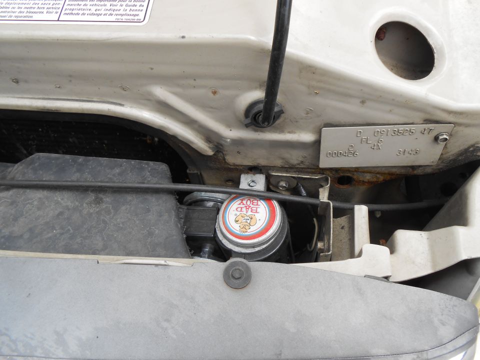 Engine bay corner with BAD BOY air horn installed near air box, stamped ID plate on beige sheet metal