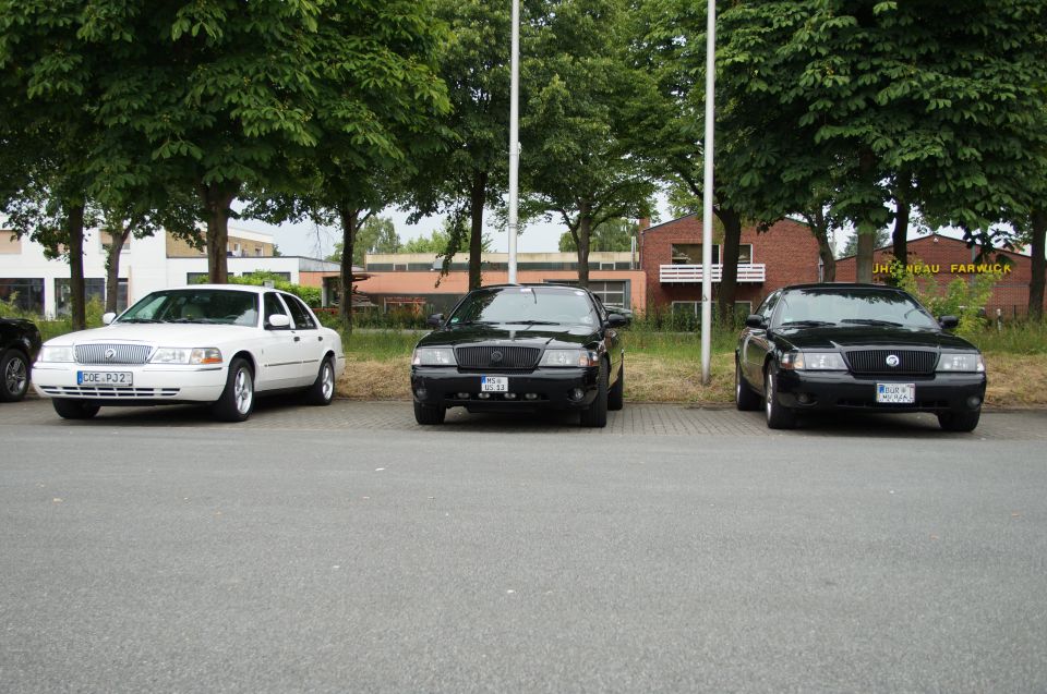 Three sedans parked in a lot, two black and one white.